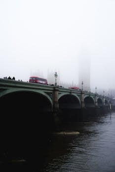 威斯敏斯特桥和大本钟的经典景观笼罩在雾中，一辆标志性的红色巴士正从旁驶过