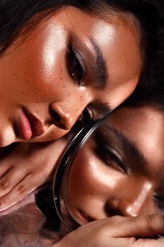 Close-up of a woman with makeup and piercing, reflected in a mirror.
