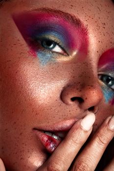 Vibrant close-up portrait showcasing colorful makeup and freckles on an expressive face.