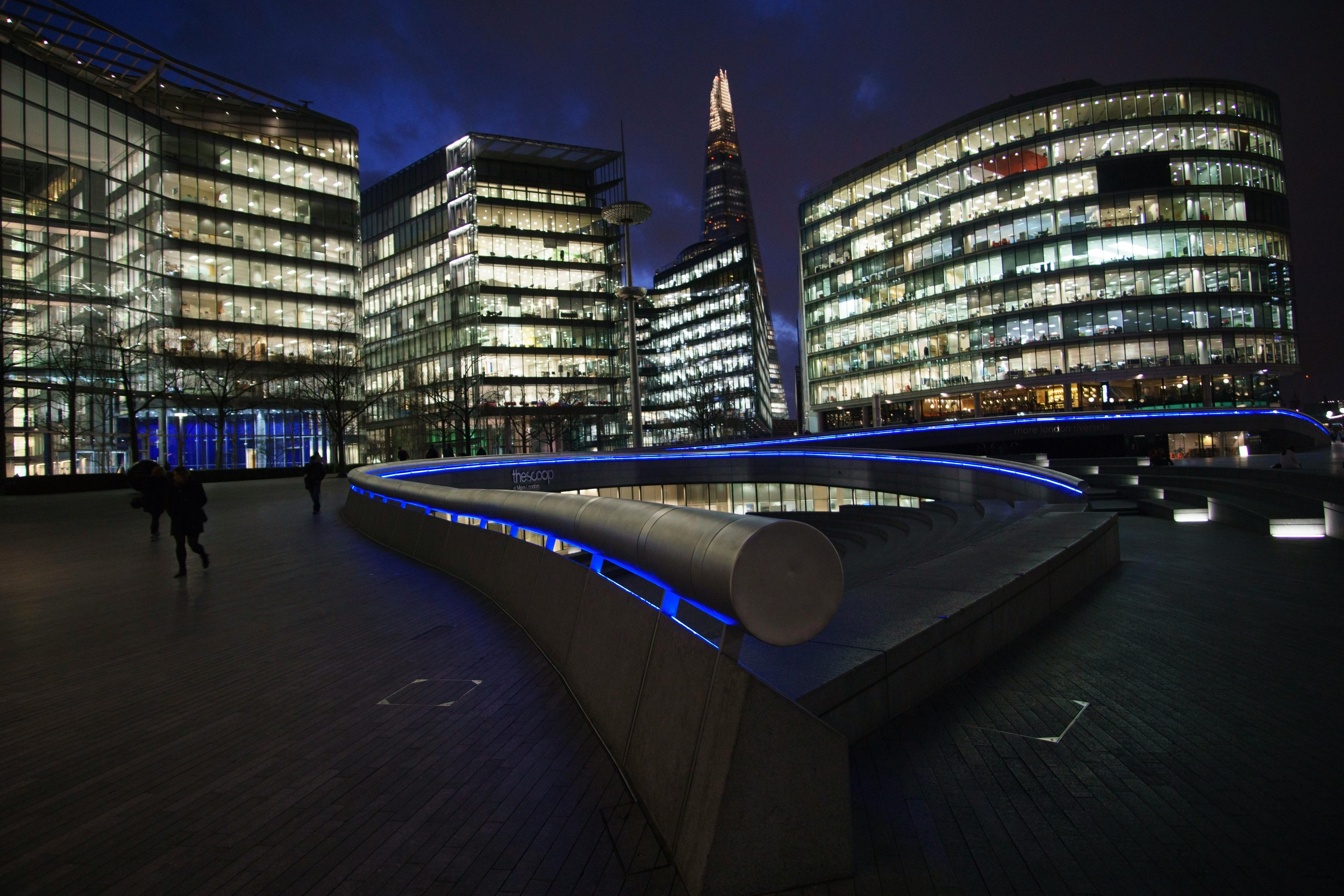 Illuminated modern buildings in London cityscape with The Shard at night.