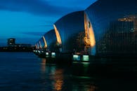 这张伦敦泰晤士河屏障的晚间照片充满活力，突显了现代建筑和温暖的灯光