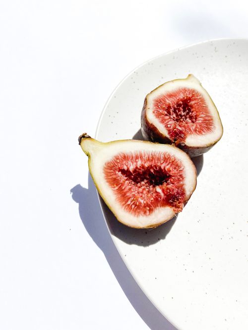 Free Sliced fresh figs on a white plate against a bright background, showcasing their juicy texture. Stock Photo