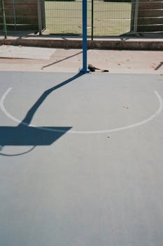 A bright outdoor basketball court with a hoop shadow creates an abstract pattern.