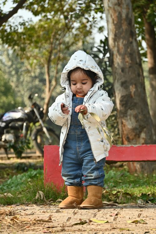 Free Cute toddler playing in a park in Moga, India, wearing denim overalls and a jacket. Perfect family moment. Stock Photo