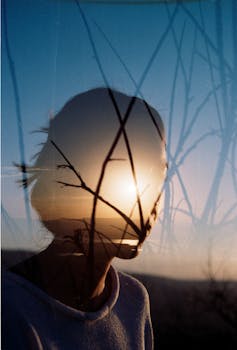 Artistic double exposure of a woman's silhouette with sunrise and branches.