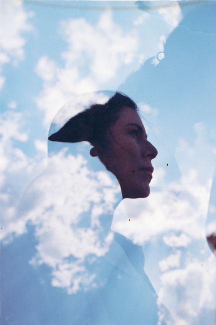 A creative double exposure portrait featuring a woman's profile against a sky filled with clouds.