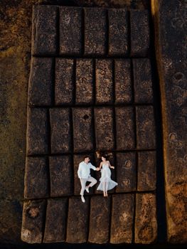 Aerial shot of a couple lying together on ancient stone blocks, showcasing love and architecture.