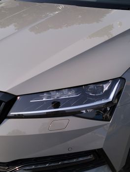 Sleek and modern car headlight and hood close-up with reflective chrome detail.
