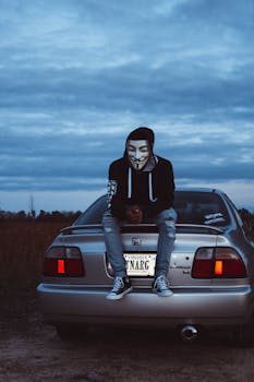 黄昏时分，在弗吉尼亚州威廉斯堡，一个戴着匿名口罩的人坐在汽车后备箱上