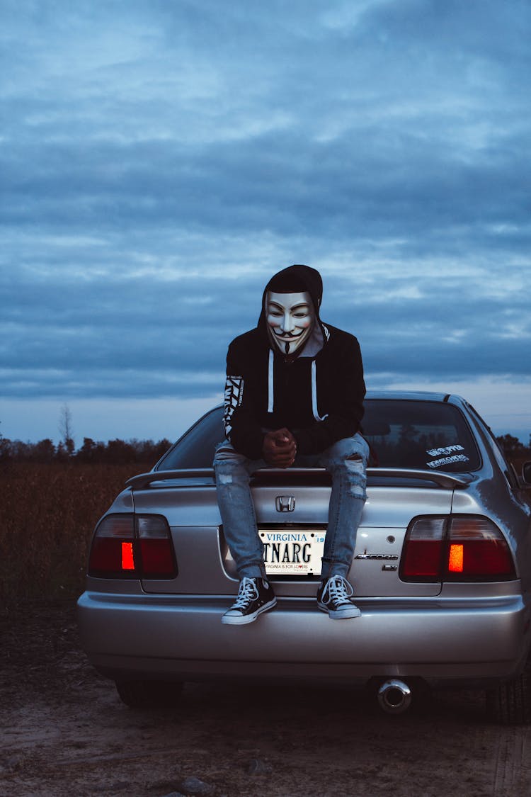 Man Wearing Guy Fawkes Mask Sitting On Gray Honda Vehicle