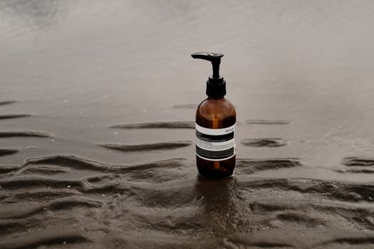 Minimalist image of a skincare bottle placed on a wet sandy beach, emphasizing tranquility.
