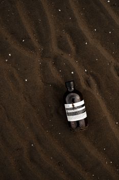 Brown cosmetic bottle resting on textured sand at a beach, evoking natural skincare themes.