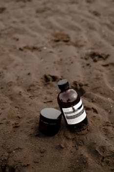 Brown bottles of cosmetic products placed on a sandy beach, conveying a natural and eco-friendly vibe.