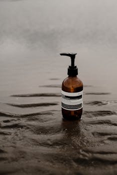 A brown cosmetic bottle with a pump on wet beach sand, emphasizing eco-friendly skincare.
