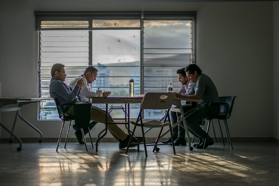 Free Four Men Sitting in Front of Table Near Glass Window Stock Photo