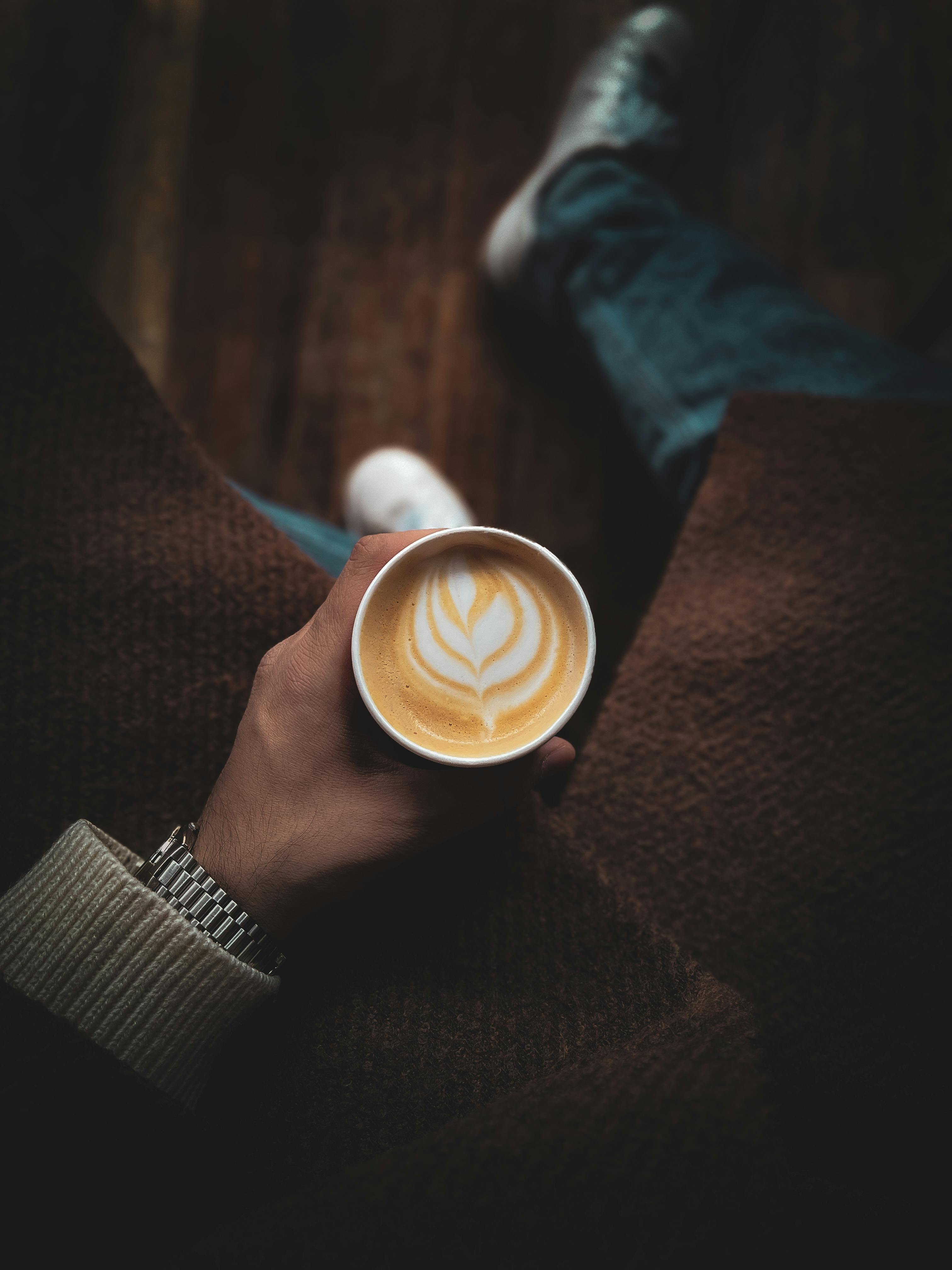A hand holds a latte with beautiful foam art, captured from above in a warm, cozy setting.