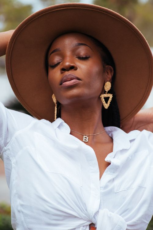 Free Beautiful woman in a hat with statement earrings enjoying a moment outdoors. Stock Photo
