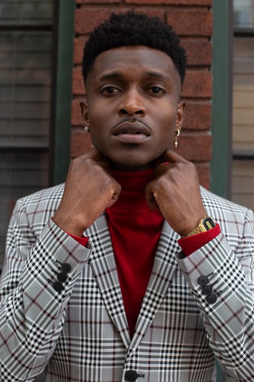 Free Portrait of a man with short black hair in a plaid suit adjusting his collar outdoors. Stock Photo