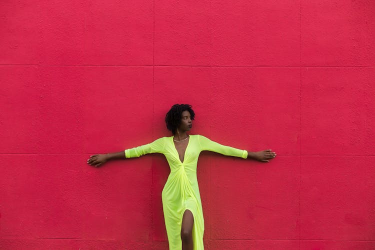 Woman Wearing A Green Summer Dress And Standing Against A Red Wall