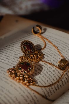 Artistic close-up of ornate golden earrings with gemstones resting on an open book.