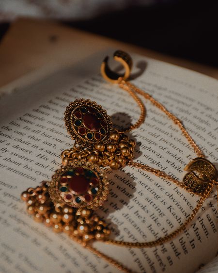 Antique gold jhumkas with delicate ear chains resting on an open book