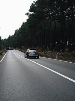 Sleek modern car traveling on a scenic forest road, showcasing vehicle and nature.