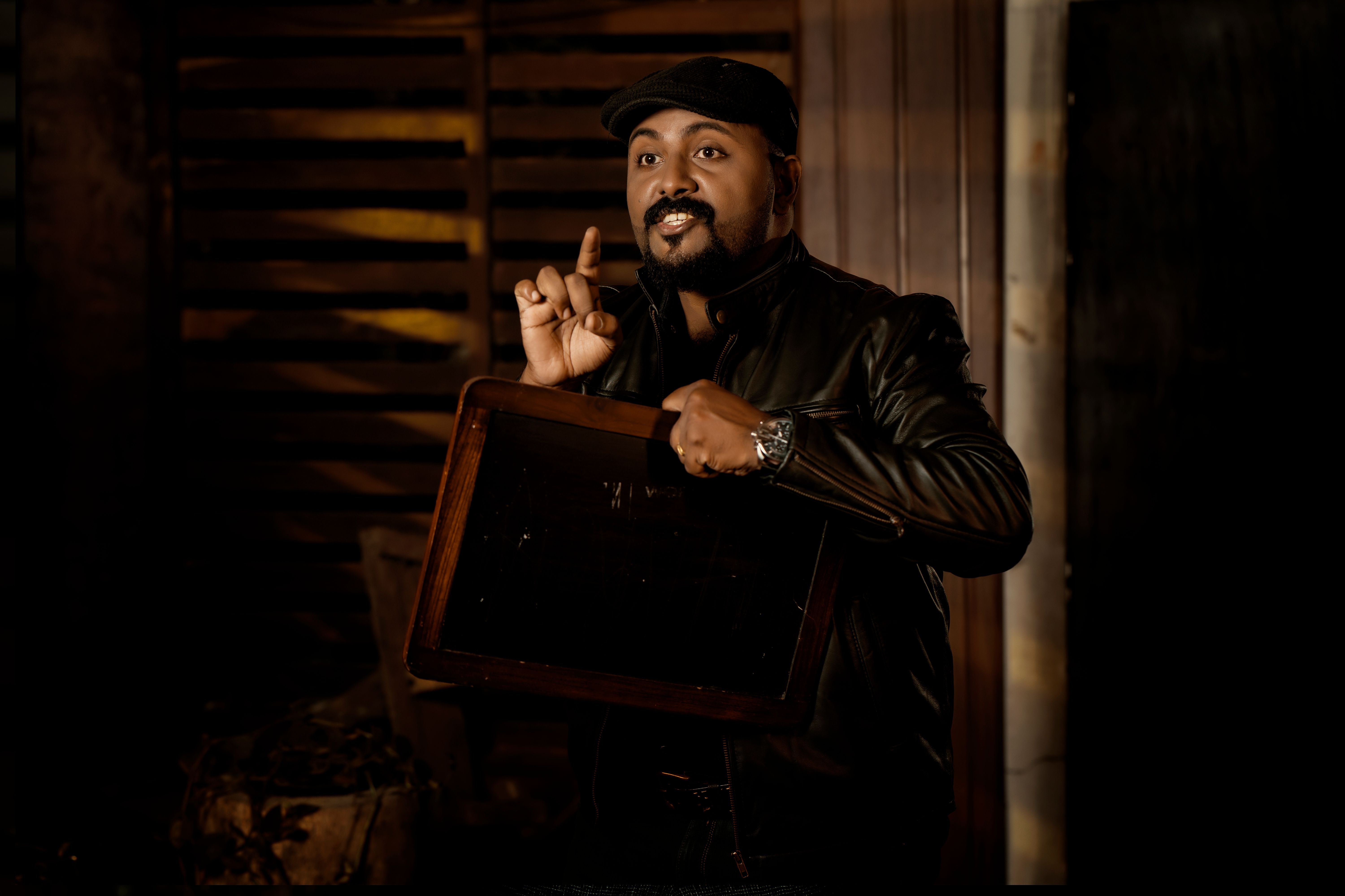 Portrait of a man in a leather jacket making a gesture indoors.