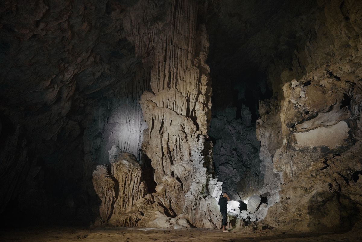 A lone explorer discovering stunning limestone formations in a dark cave.