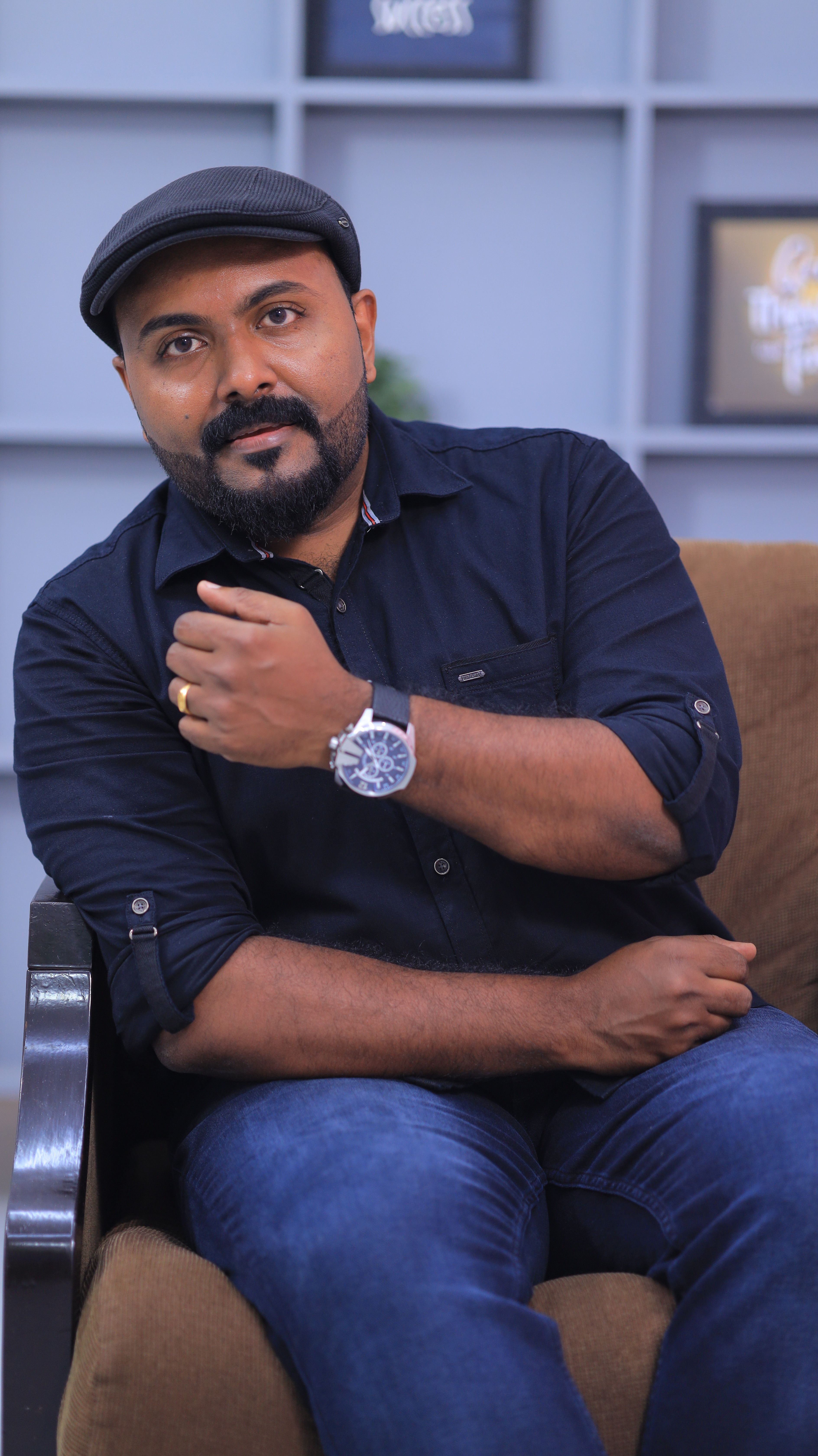 Casual portrait of a man with a beard and wristwatch sitting indoors, exuding a fashionable vibe.