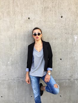 在希腊塞萨洛尼基，一名穿着时尚休闲装的年轻女子靠在混凝土墙上摆姿势