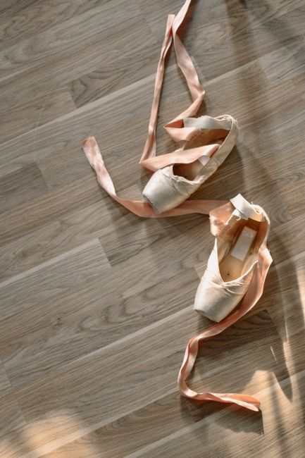 Top view of ballet pointe shoes with ribbons on a wooden floor, capturing elegance and artistry.