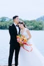 新郎和新娘优雅地在湖边手持色彩缤纷的花束摆姿势