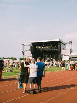 Crowds enjoy a sunny day at an outdoor music festival with a large stage and relaxed atmosphere.