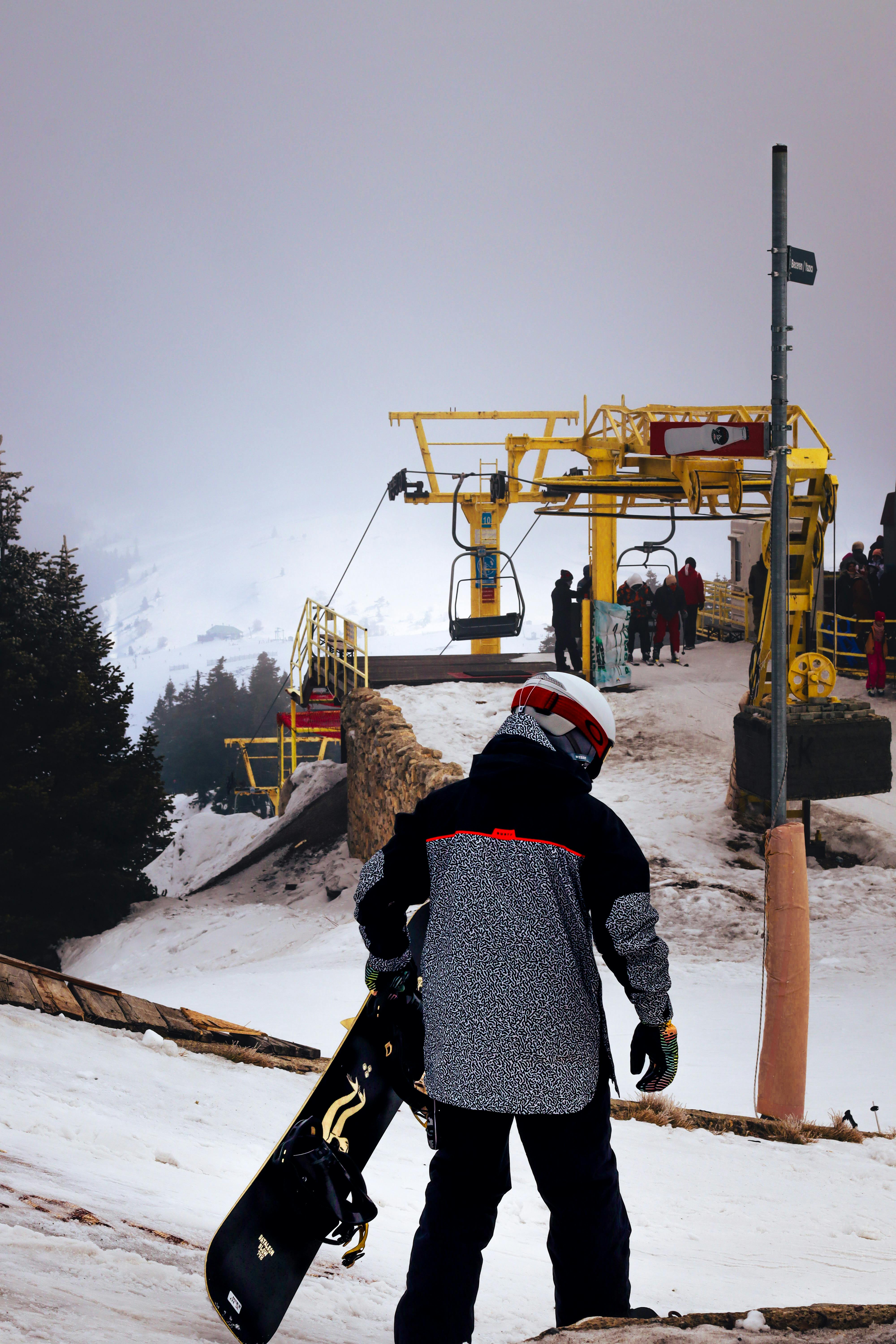 Prescription Goggle Inserts - Snowboarder walking towards ski lift on a snowy mountain slope during winter, with others waiting.