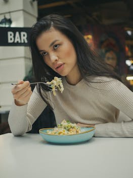 Young woman dining indoors with pasta in a casual restaurant setting.