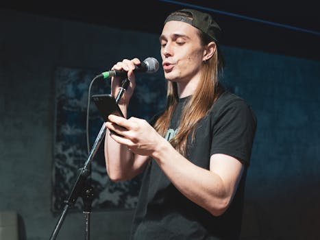 A young man performs passionately on stage holding a microphone and smartphone, set indoors.