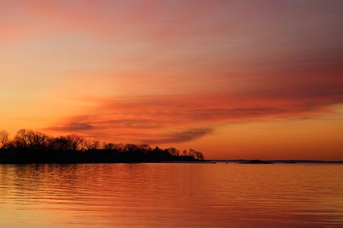 Free Breathtaking sunset view over a calm lake with silhouetted trees, capturing nature's vibrant colors. Stock Photo