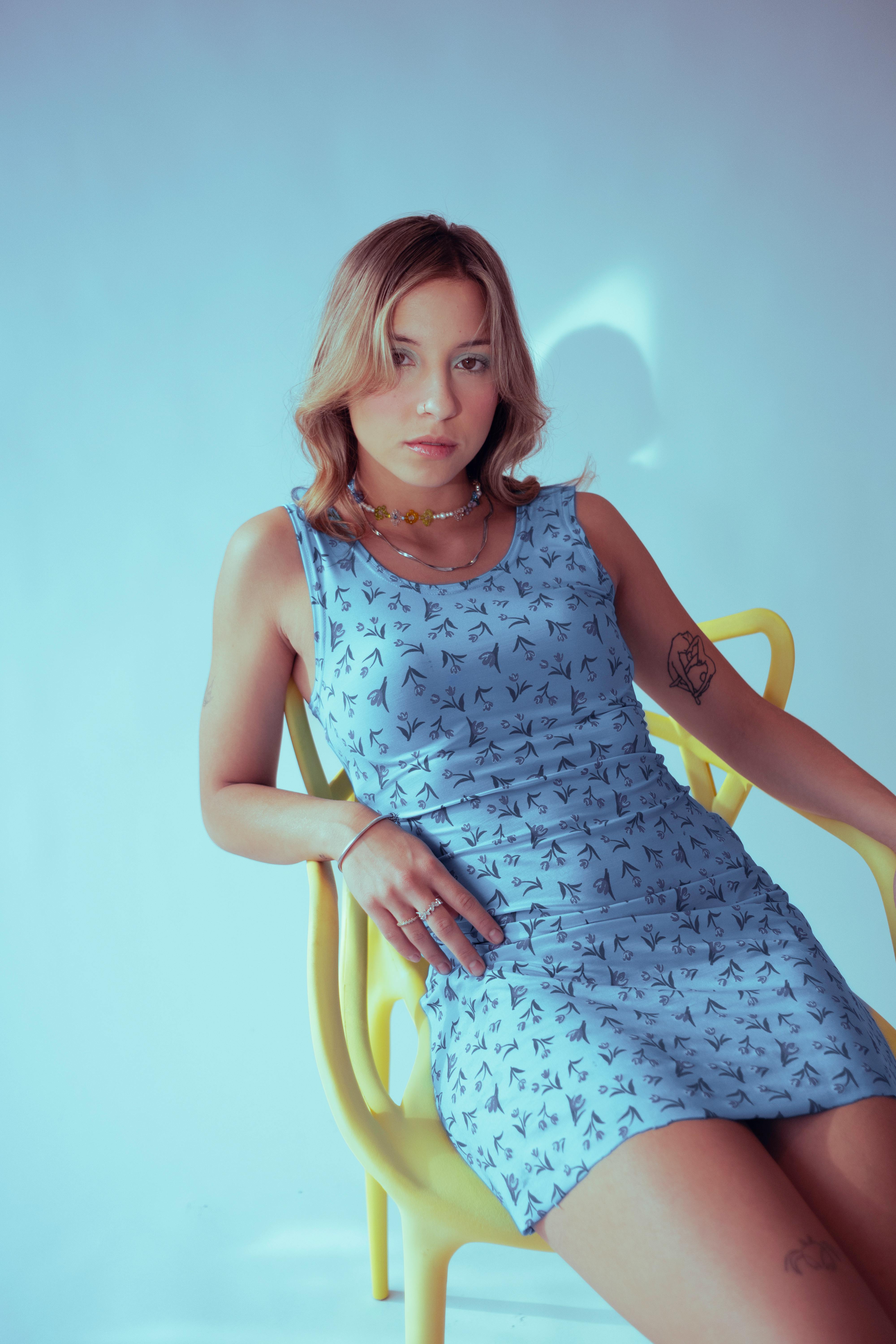 一位穿着蓝色连衣裙的年轻女子坐在黄色椅子上的优雅肖像，散发着现代时尚的气息
