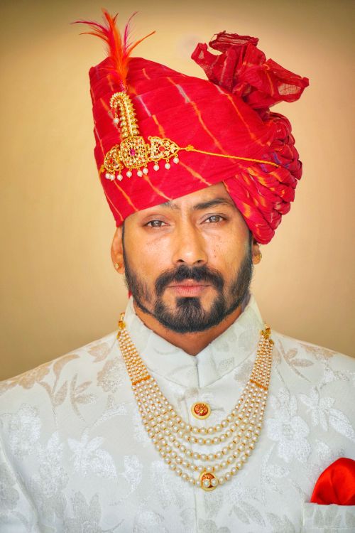Free Portrait of a refined Indian groom with a red turban and traditional accessories. Stock Photo