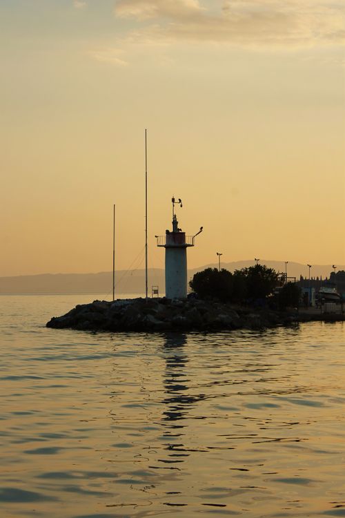 Free A peaceful sunset scene featuring a lighthouse and its reflection over tranquil waters. Stock Photo