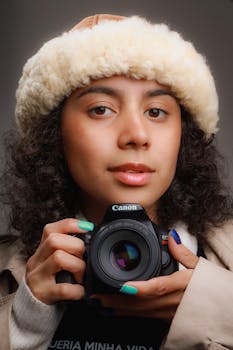 Close-up portrait of a young woman holding a camera with a winter hat, shot in SP, Brazil.