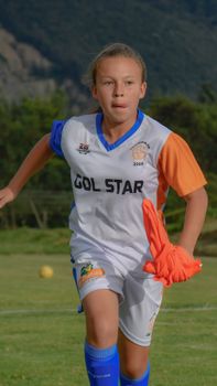A determined young girl playing soccer on the field wearing a Gol Star jersey.