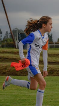 A young female soccer player running on the field during training session outdoors.