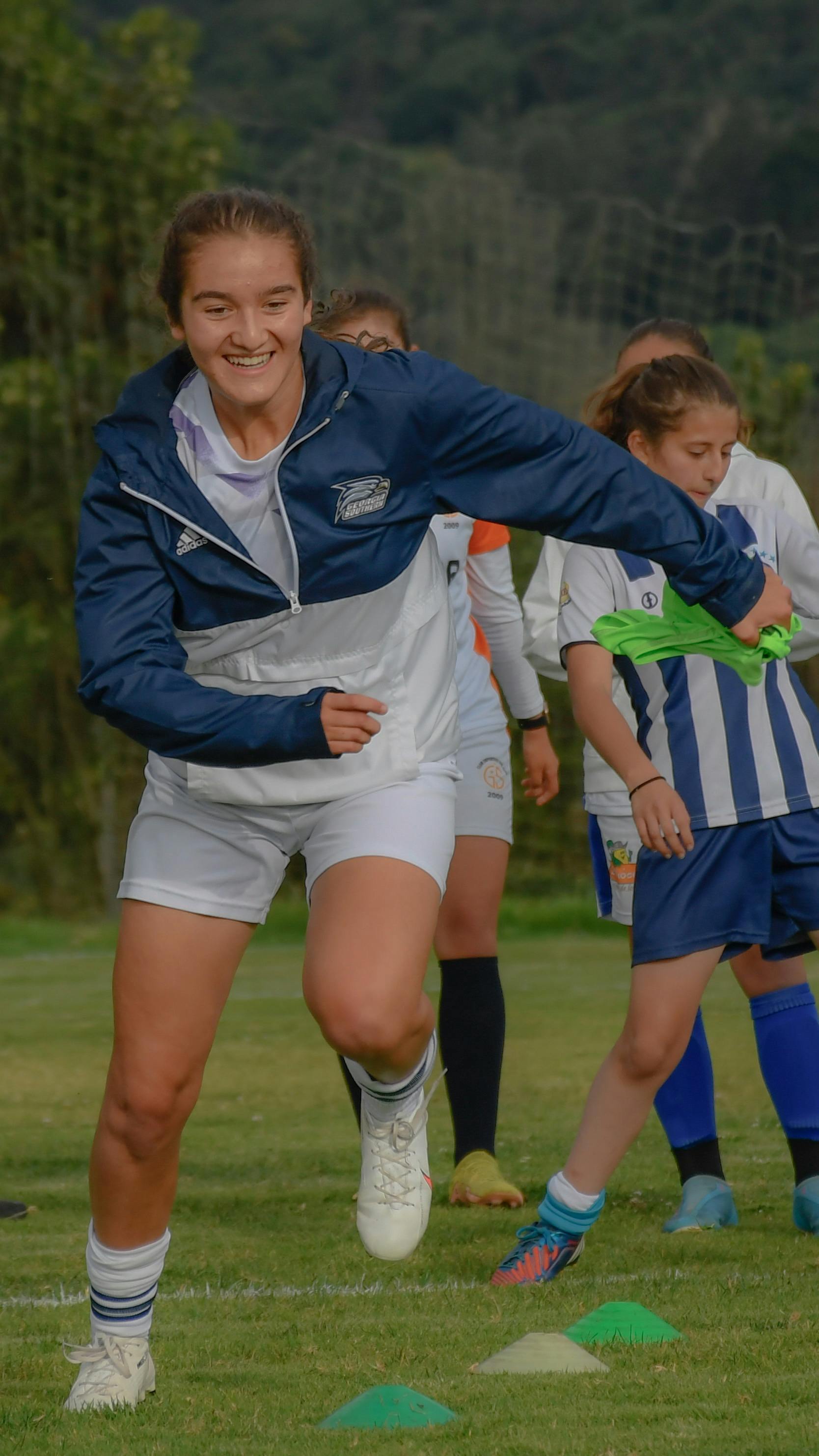 smiling woman in sports clothing running on grass