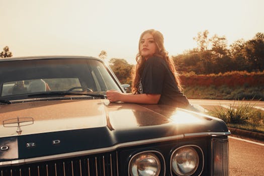 A woman poses on a vintage Ford car at sunset, showcasing style and classic automotive design.
