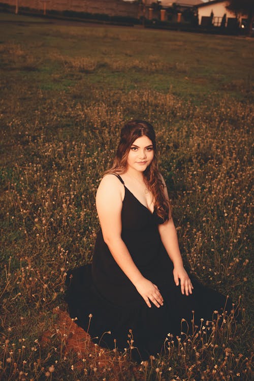 Woman in Black Dress Sitting and Posing on Meadow