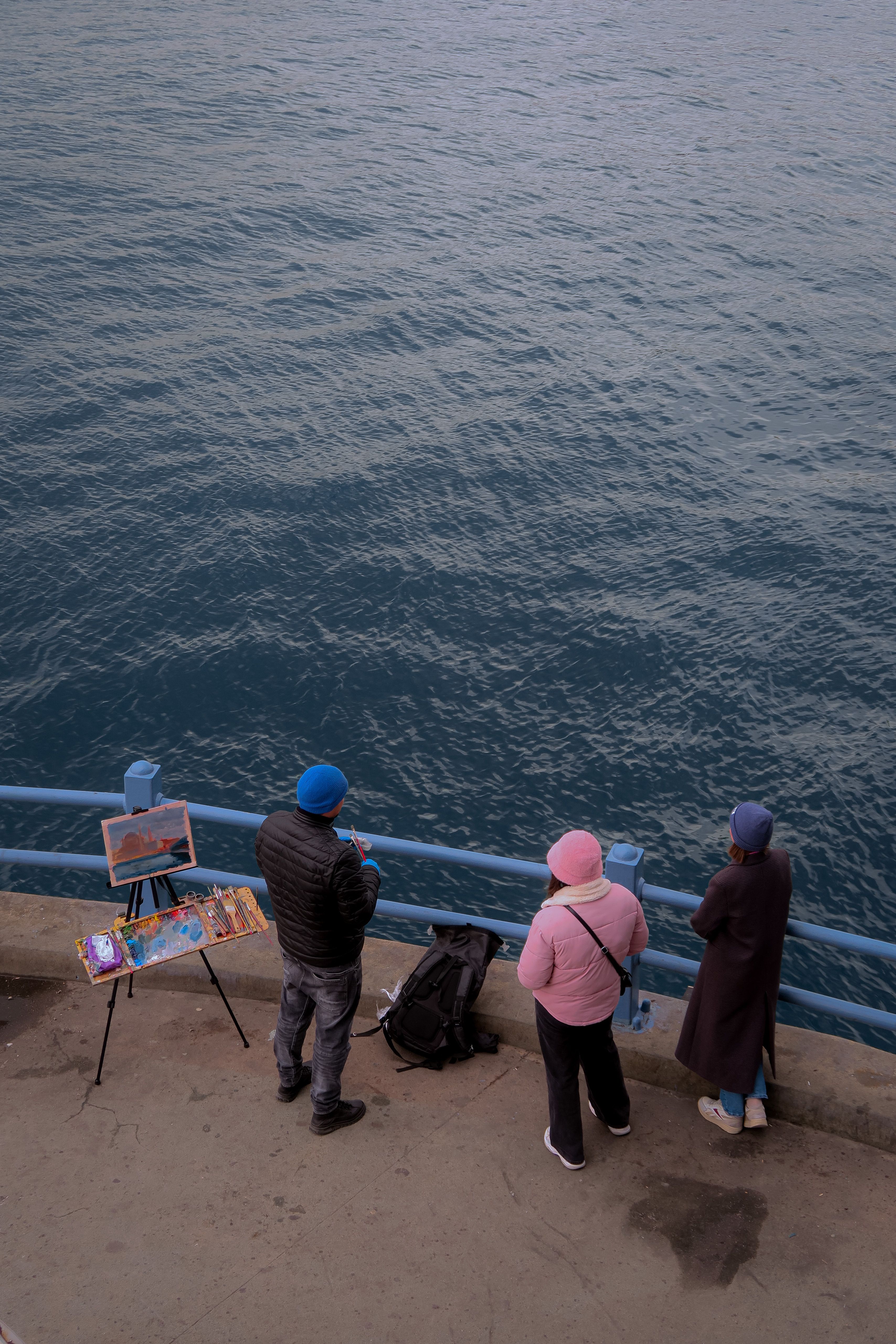 A high angle view of people standing on a pier, dressed for cold weather, looking at the water.