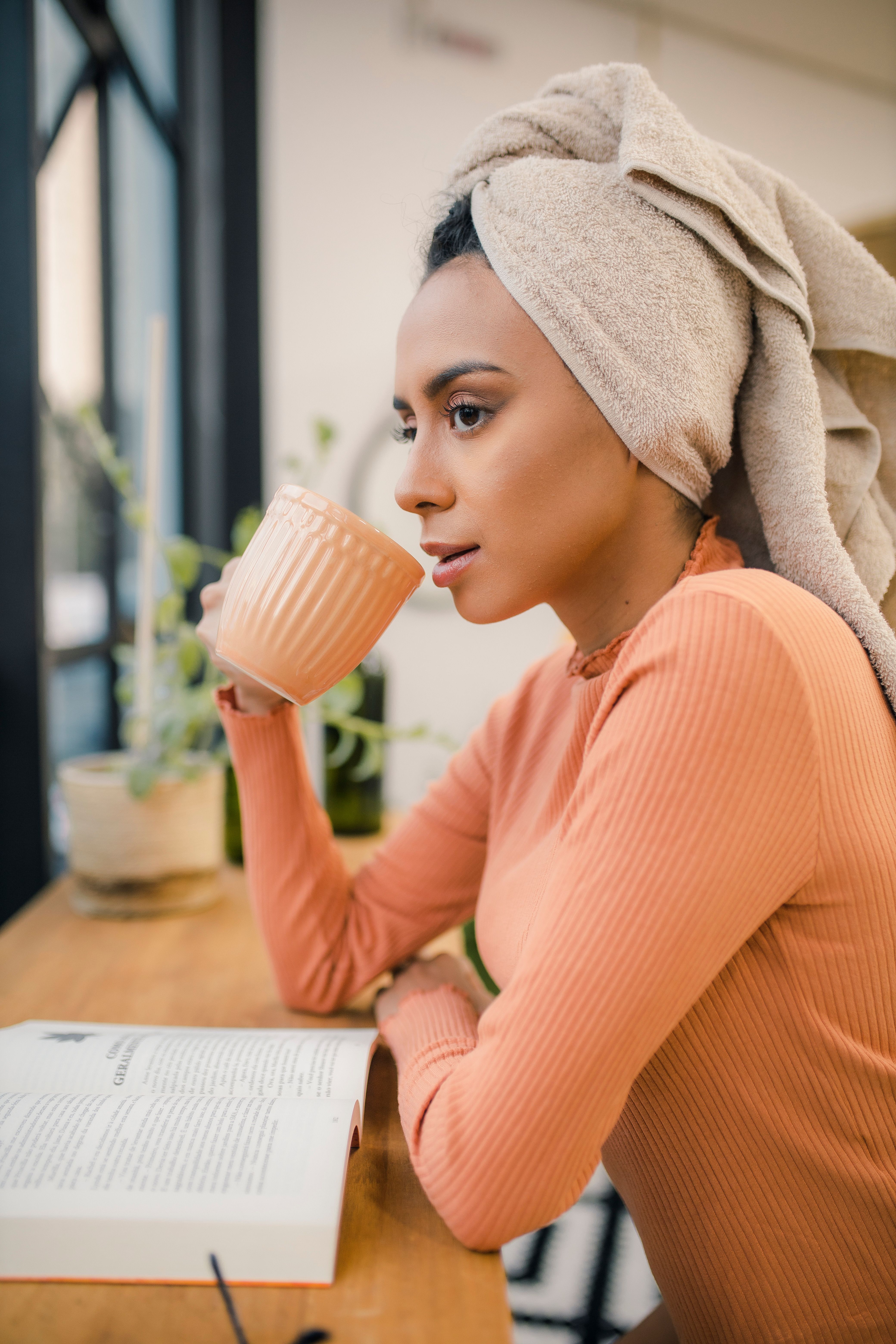 A young woman in a pink sweater enjoys coffee while reading a book indoors, captured in a serene moment.