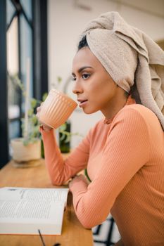 A young woman in a pink sweater enjoys coffee while reading a book indoors, captured in a serene moment.