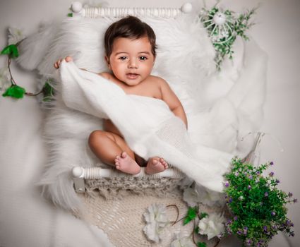 A cute baby lying on a fluffy white blanket surrounded by vibrant greenery and flowers.